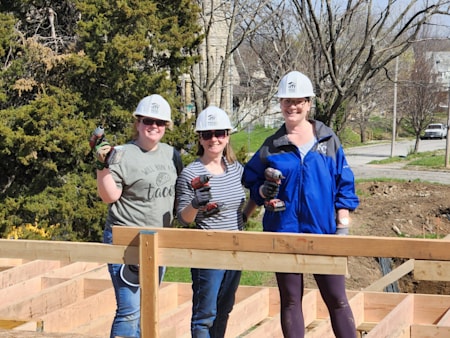 A team of First Business Bank’s Kansas City Metro employees wearing construction hats and holding power drills on a sunny spring day